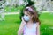 Girl teenager in protective medical mask in the spring among blooming garden. Quarantine coronavirus in Europe. Allergy to