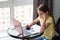 Girl thoughtfully doing homework, sitting at a table by the window