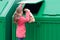 Girl throws out a paper bag in a green dumpster