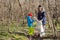 A girl throws a plastic bottle into a trash bag that the girl holds, together they collect garbage in the forest