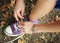 A girl ties white laces on lilac sneakers, close-up, against a background of grass and leaves, top view.