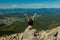 The girl at the top of the mountain raised her hands up. Wide summer mountain view at sunrise and distant mountain range covered.