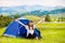 Girl tourist meets morning with outstretched arms in tent with beautiful mountains view