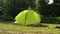 Girl tourist sets up the tent against the green forest. Throws on and adjusts the light green awning. Sports rest