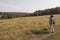 A girl tourist shows on something in a field with a forest.