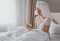 Girl with a towel on her head sits on a white bed in a hotel