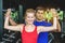 The girl is training dumbbells flexing muscles with help of her personal trainer in the gym