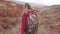 Girl traveler with a backpack walking along the mountainous terrain. back view. red mountains and red earth as on Mars.