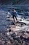 Girl traveler crossing a mountain fast river over a crossing over rocks