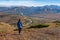 Girl traveler on the edge of the cliff looking at the plain and mountains, green and orange hills