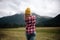 Girl traveler in hat with backpack looking at clouds in mountains