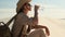 girl traveler in safari clothes sits on sand dune in the desert and drinks water