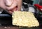 The girl tries to bite off a piece of dry Chinese instant noodles, which is lying on a baking sheet from the oven