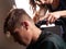 A girl with a trimmer straightens the hair on the back of the head to a man at the hairdresser