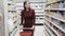 Girl with trolley goes among shelves with goods in grocery store, steadicam shot