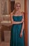 Girl in a turquoise dress stands in the doorway leading to the bathroom and looks at the camera