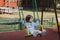 Girl two years old brunette in a dress and jacket swinging on a swing