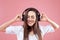 Girl uses wireless earphones. Beautiful young woman in wireless headphones listening to music on pink background.