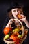 A girl in a vampire costume with yellow eyes holds a basket with vegetables. Bright emotion. Conceptual photo