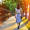 Girl walking away through green alley at the sunset