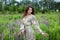 Girl walking on field on summer with wildflowers. Woman in long dress stands in blooming purple lupine field. Beautiful girl with