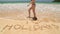 Girl walking in front of word holidays written in sand on beach just before ocean wave covers it