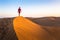 Girl walking on sand dunes in arid desert at sunset and wearing dress, scenic landscape of Sahara or Middle East