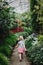 girl walking on stone path in botanical garden greenhouse with green trees, plants and colorful flowers