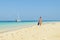 Girl walks on the beach with snorkelling gear with catamaran in