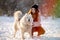 A girl walks with her beloved pet Samoyed in winter on the shore of a lake in the park.