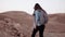 Girl walks near mountain drop. Slow motion. Young female tourist on desert canyon edge. Big rocks and stones. Israel.