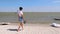 The girl walks slowly along the sandy beach and looks at the sea. Background made of silhouettes of people engaged in