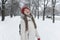 Girl walks through the snow-kept park and catches snowflakes with her tongue. Young woman in red hat in winter outdoors