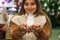 Girl in warm coat holding glass ball with firtrees, house and artificial snow in a mall at the Christmas Fair. Winter mood