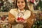 Girl in warm coat holding glass ball with firtrees, house and artificial snow in a mall at the Christmas Fair. Winter mood