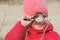 A girl in warm red clothes with a magnifying glass in her hand examines a tree branch .  Winter outdoor kids activity concept