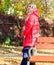 Girl wear red bright warm jacket. Fall fashion concept. Lady attractive posing in jacket near bench. Woman fashionable