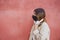 Girl wearing a black reusable mask against coronavirus with white headphones with a red wall