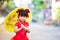 Girl wearing red cheongsam walks yellow vintage umbrella  a sweet smile. Child looking at camera.