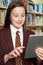 Girl Wearing School Uniform Using Digital Tablet In Library
