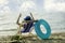 Girl wearing wide brim sun hat sitting on deck chair outdoor by the beach with coconut and blue lifebuoy , with sunshine bright