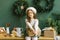 Girl in a white beret sits in a stylish kitchen decorated for Christmas and New Year in emerald or green. Christmas wreaths on the