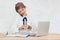 Girl in white blouse sits at table with laptop and looks at clock