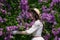 Girl in a white dress hugs a flowering lilac in the park