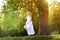 A girl in a white dress rides on a swing in nature and the horse grazes in the meadow.