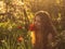 Girl in white dress smelling tulip in sunset among fluff, dandelions and cherry flowers