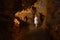 A girl in a white dress stands in a cave. Ancient formations of stone. Touristic hiking route. Concept of excursions and