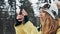 A girl in a white hat and a snowboard mask in the forest photographs nature on the phone in winter