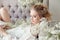 Girl white light dress and curly hair, portrait of woman with flowers at home near the window, purity and innocence. Curly blonde