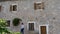 Girl with white long shirt sending a message in smart phone and stone house with flowers in the facade. Woman typing in cell phone